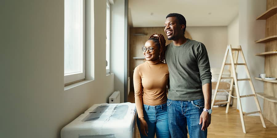 A happy young African American couple standing in a living room being remodeled.
