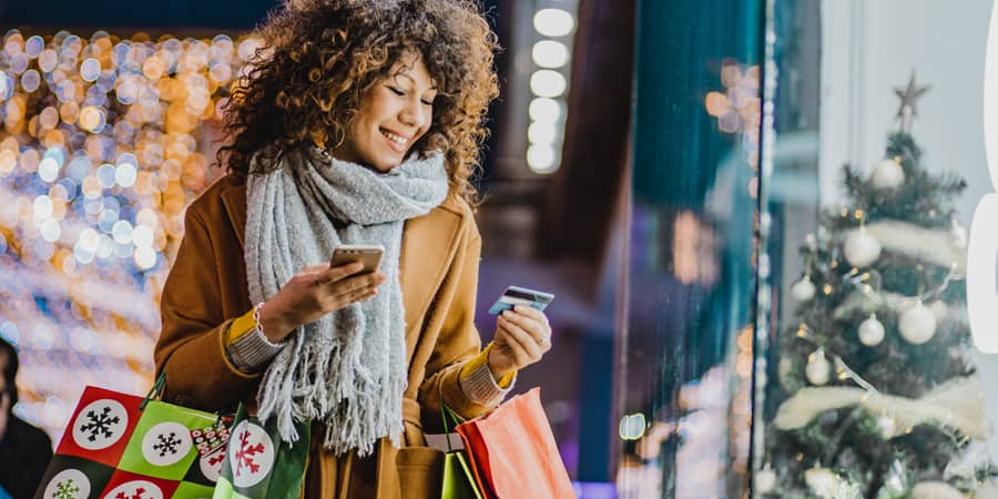 A woman carrying shopping bags while holding a credit card.