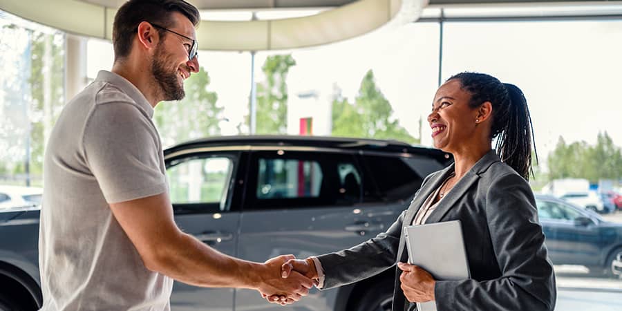 A man and a woman standing in a dealership shaking hands.