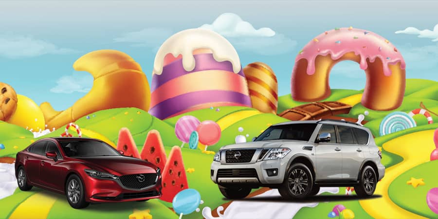 A red sedan and a silver SUV parked against a backdrop of giant, colorful donuts and cupcakes.