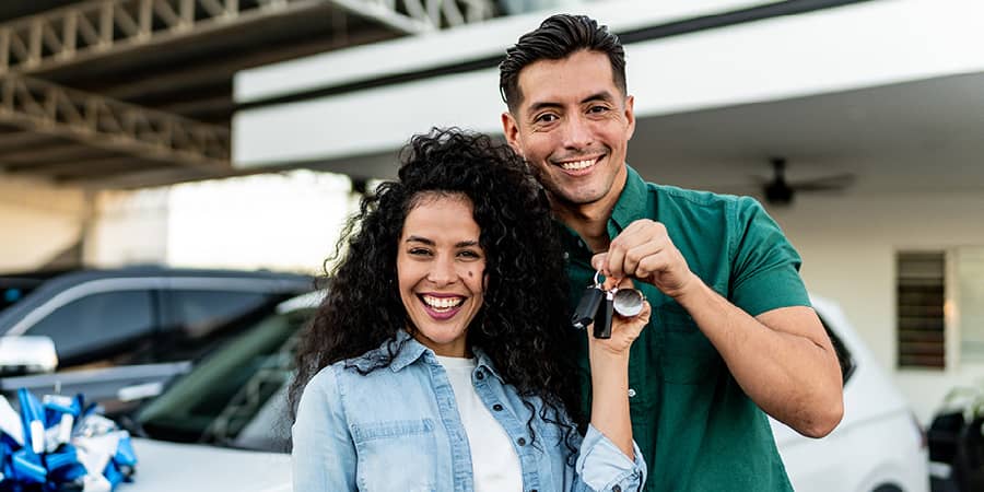 A young couple sitting in a new car with the female holding car keys.