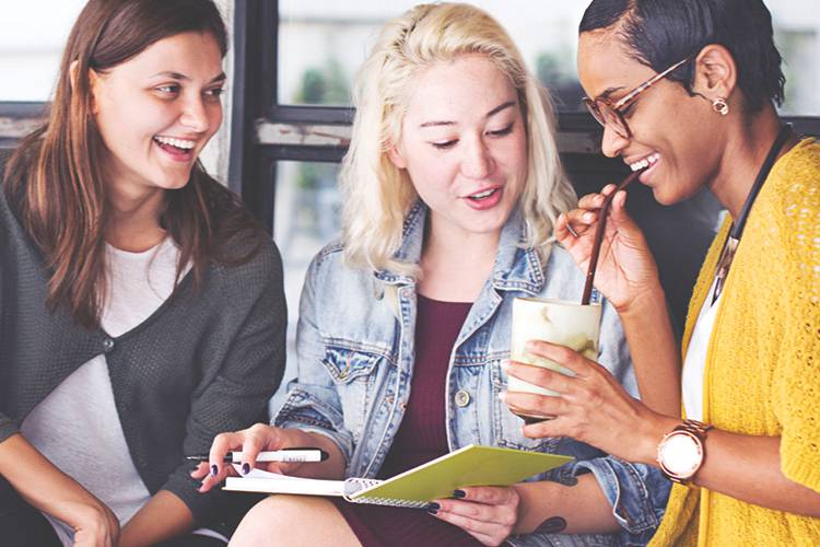 Three woman sitting together looking at a notebook and smiling