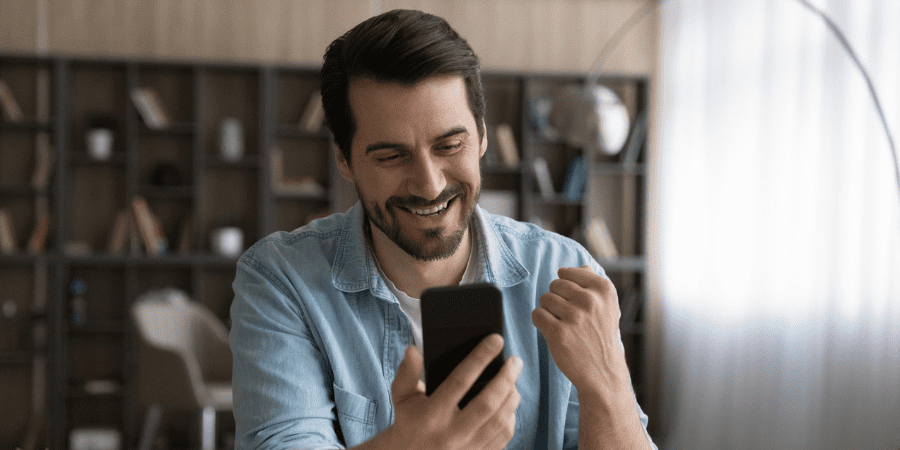 A man smiling while holding and looking at a mobile phone.