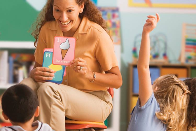 Teacher holding flash cards in front of students with raised hands