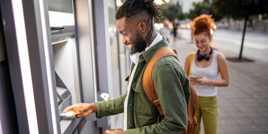 A smiling young African American man using an ATM machine.