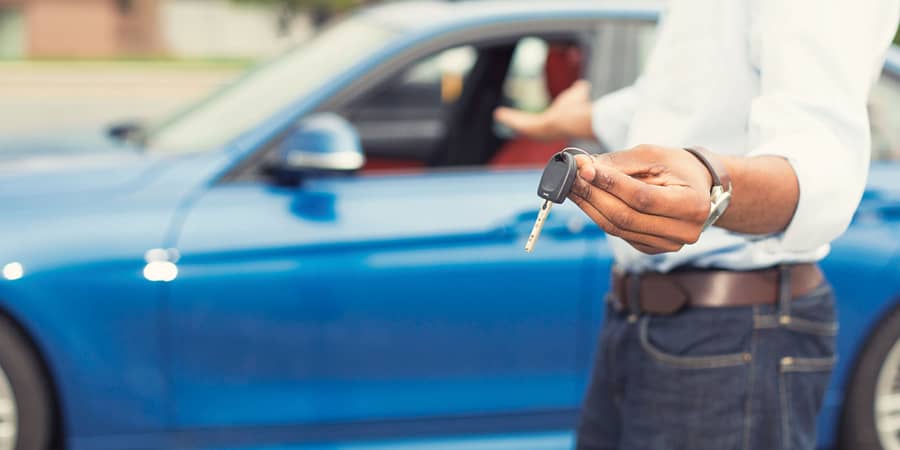 A man holding car keys while extending his hand towards a car.