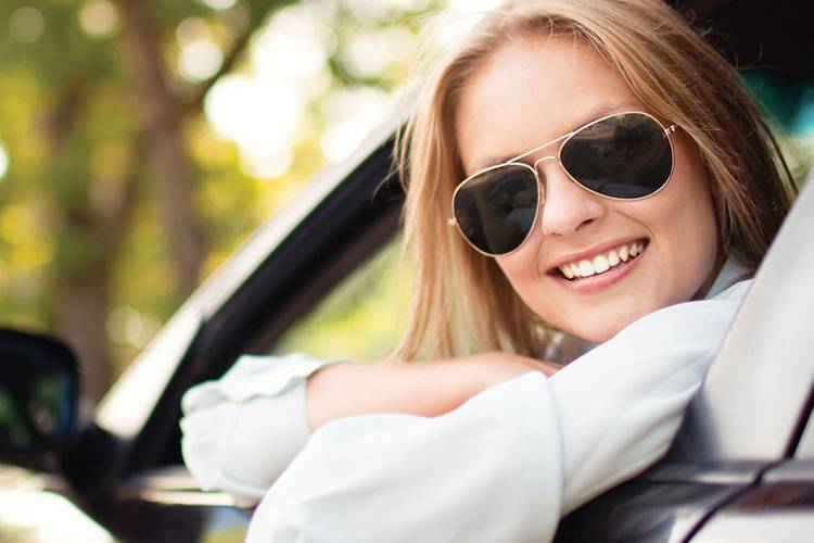 Woman smiling sitting in her car with sunglasses