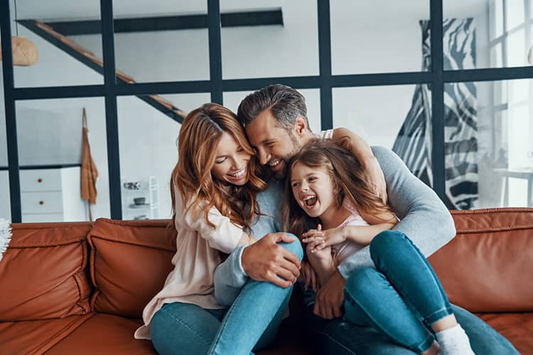 A family of three hugging on a couch in a modern living room.