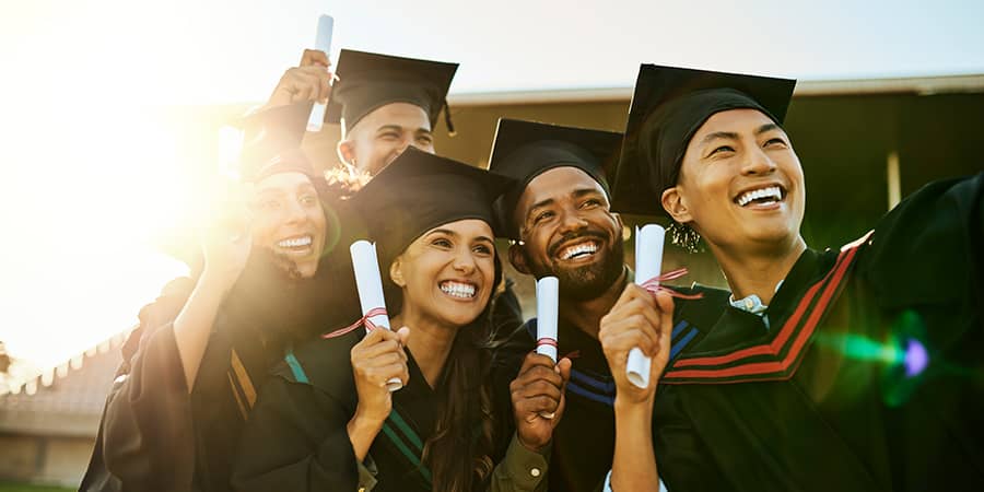 A crowd of students wearing graduation gowns and throwing their graduation caps in the air.