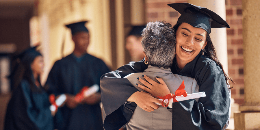 A female graduate embracing an elderly woman.