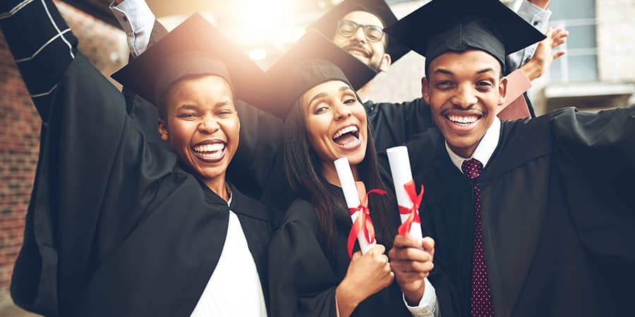 A group of happy graduates holding diplomas wearing graduation gowns.